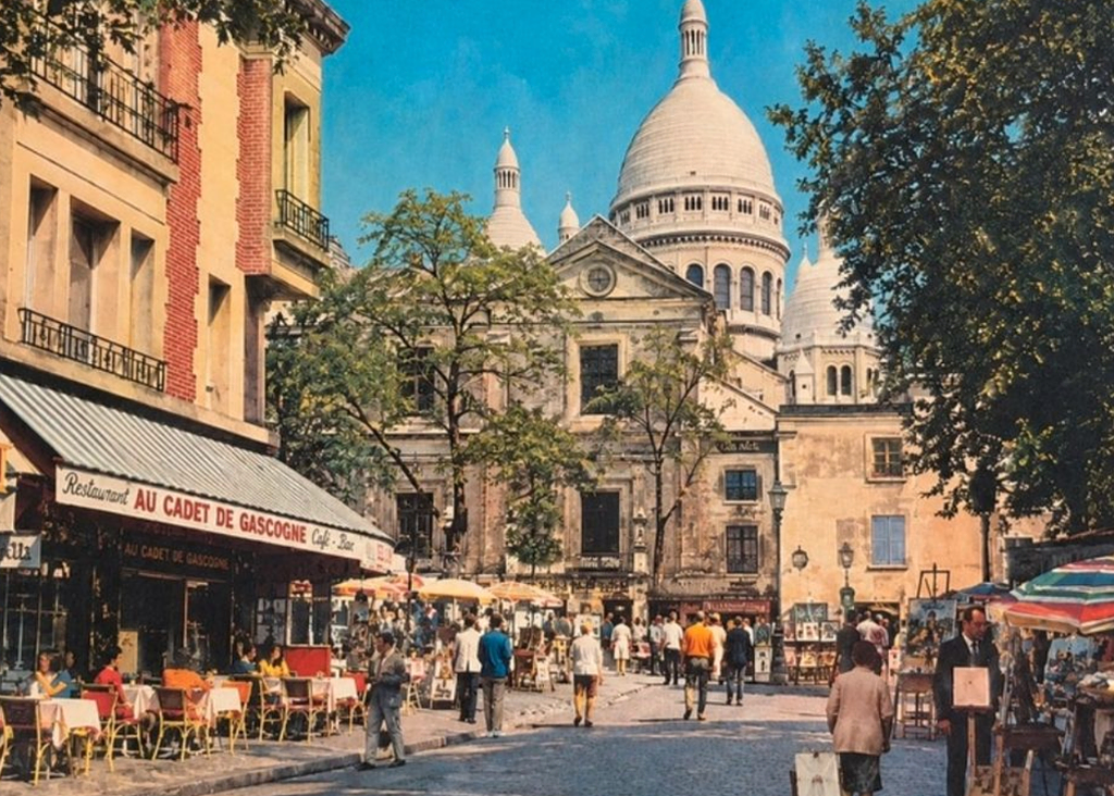 Carte postale ancienne : la place du Tertre à Montmartre, ses terrasses et ses peintres, avec le Sacré-Cœur en arrière-plan